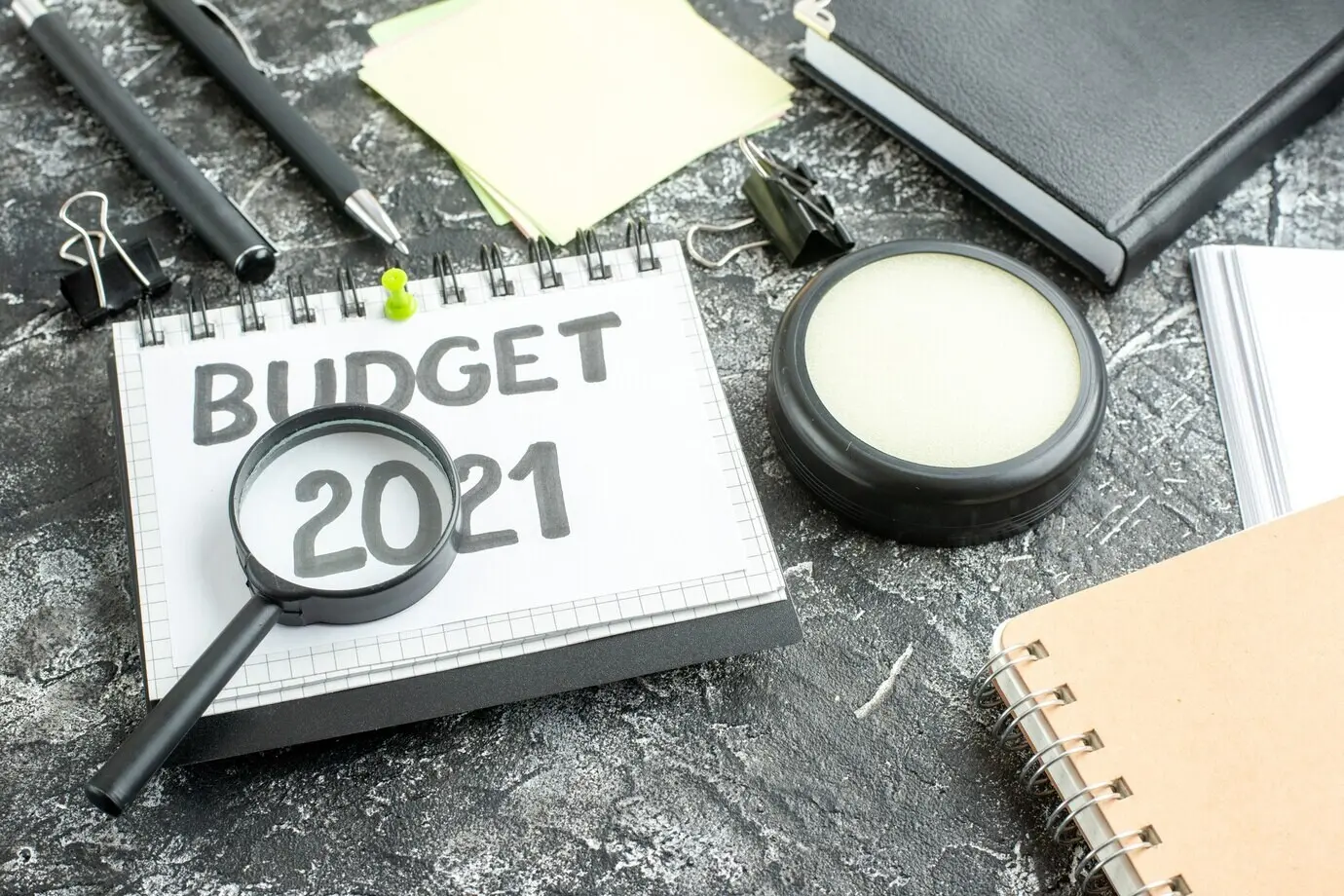 Overhead view of a budget note with a magnifier on a dark background.