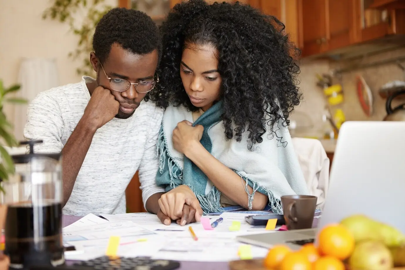 A young dark-skinned couple handling their finances, seated at the kitchen table, looking stressed.